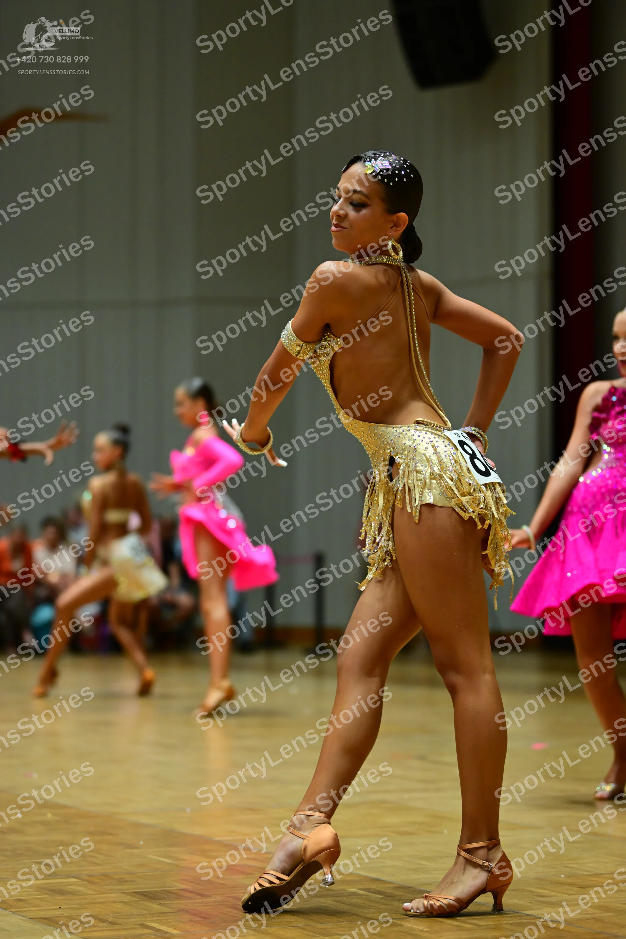 Dancesport competitor: Female dancer in foreground: gold sequined Latin dance costume with a backless d