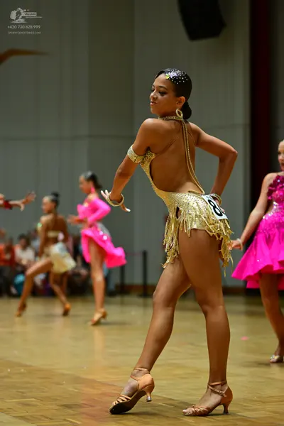 Dancesport competitor: Female dancer in foreground: gold sequined Latin dance costume with a backless d
