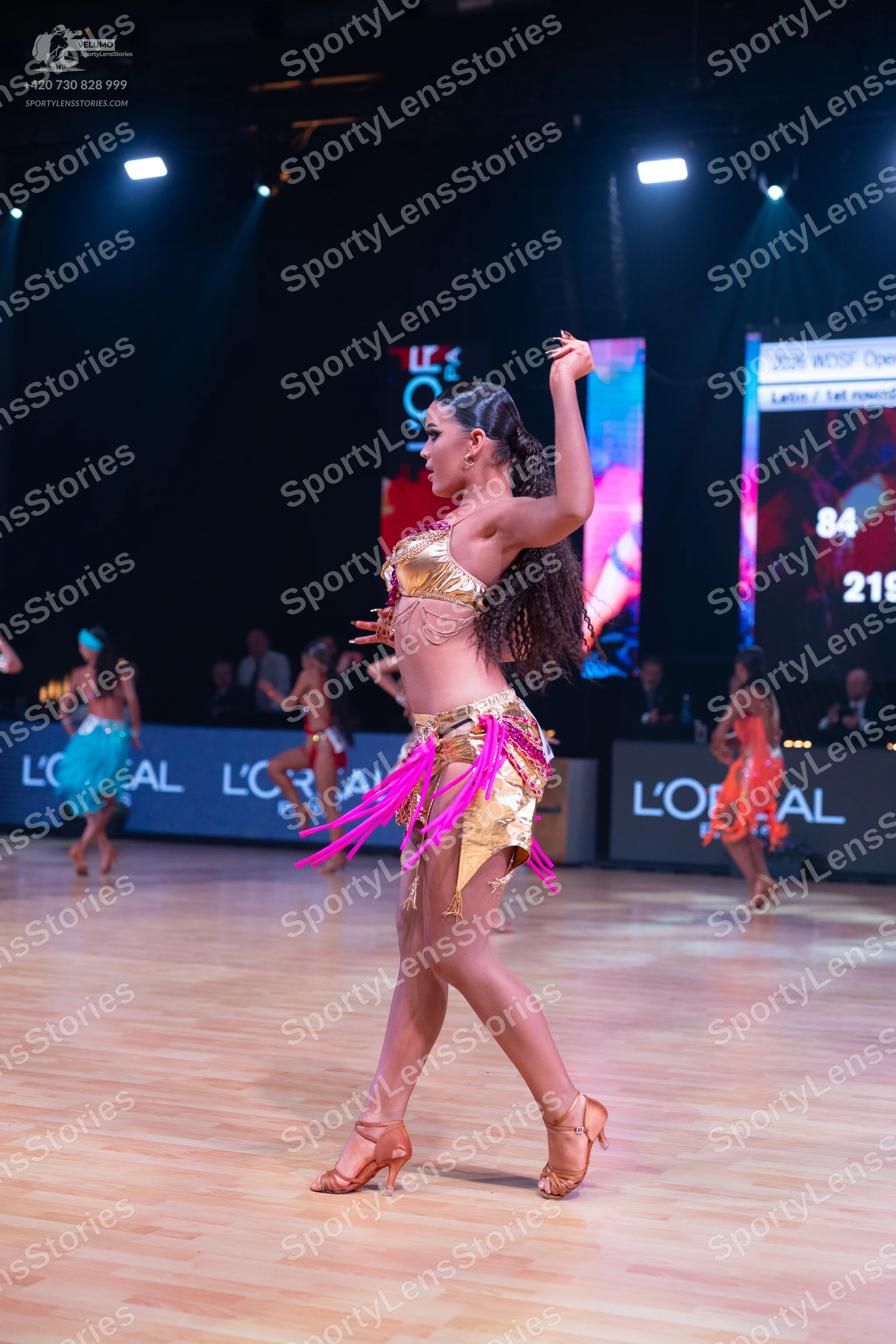 Dancesport competitor: Female dancer in foreground: gold sequin latin dress with long pink fringe
