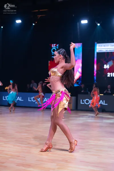 Dancesport competitor: Female dancer in foreground: gold sequin latin dress with long pink fringe