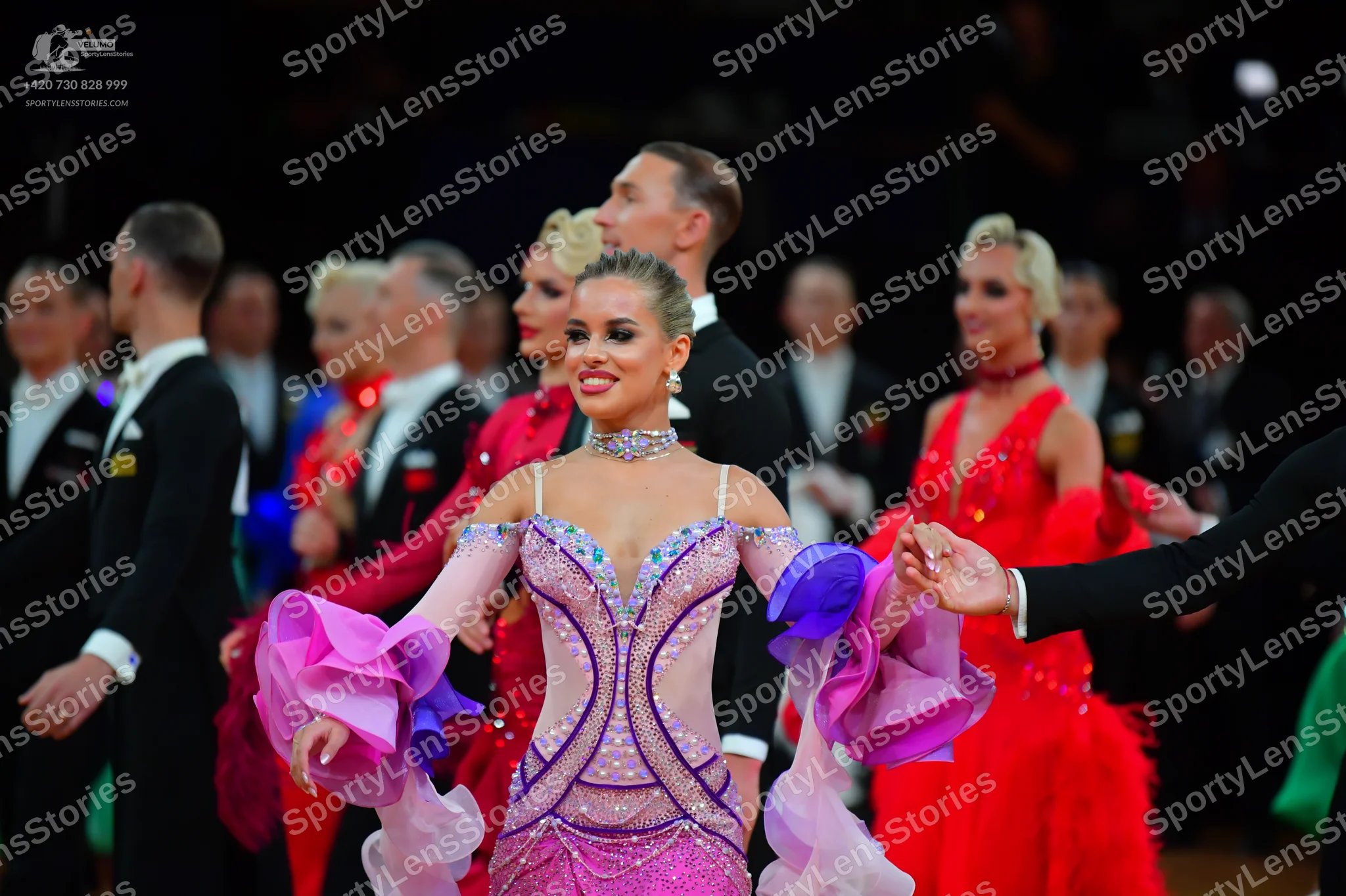 Dancesport competitor: Female dancer (foreground): lavender and pink sequined latin dress with large, c