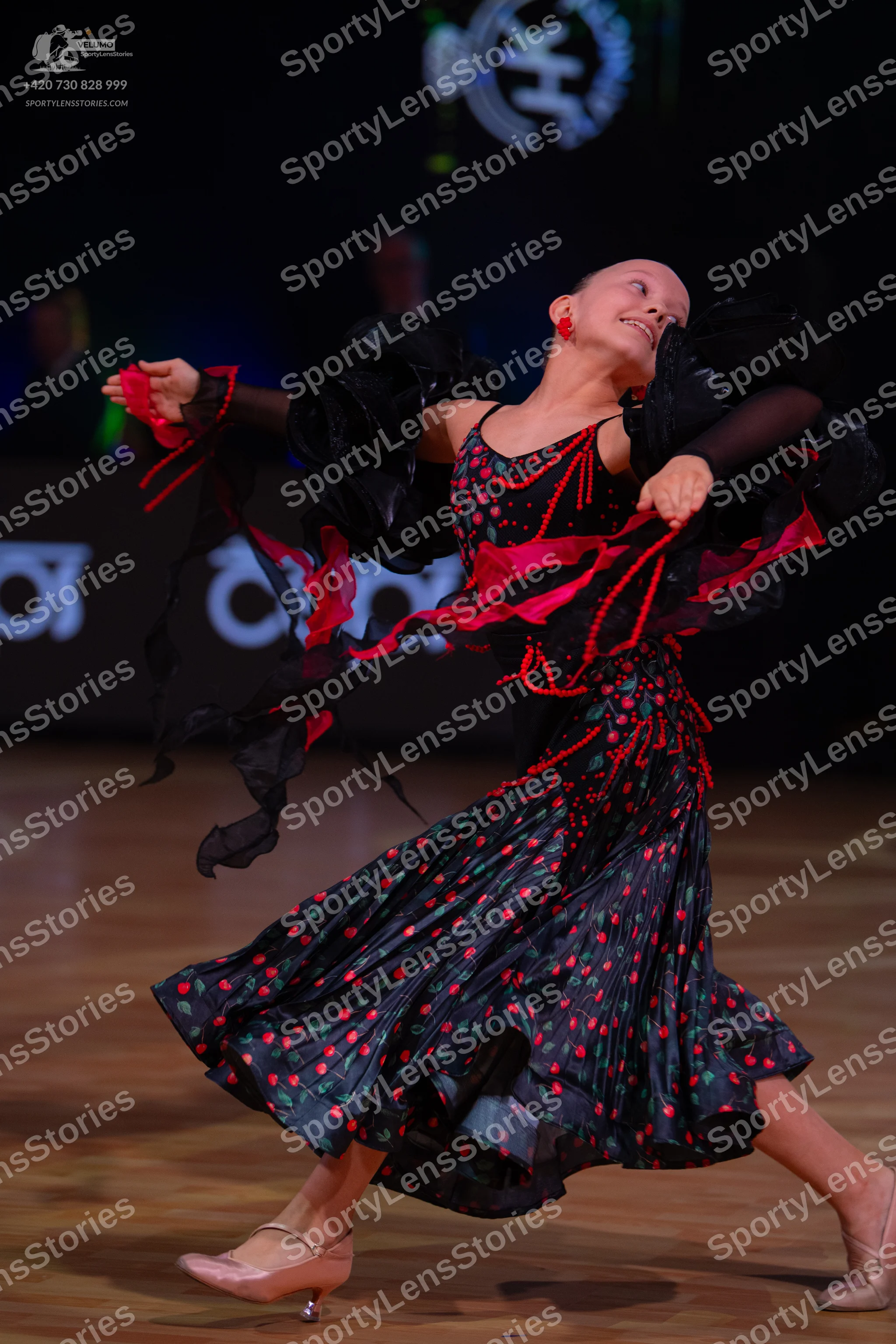 Dancesport competitor: Female dancer: black ballroom dress with red patterns, large black ruffles on th