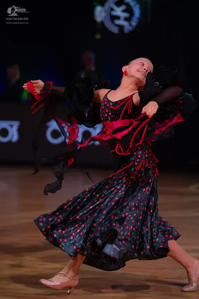 Dancesport competitor: Female dancer: black ballroom dress with red patterns, large black ruffles on th