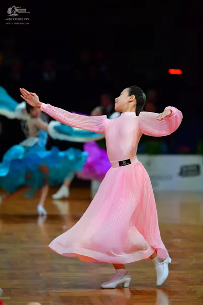 Dancesport competitor: Foreground dancer: light pink long-sleeved ballroom dress with pleated fabric on