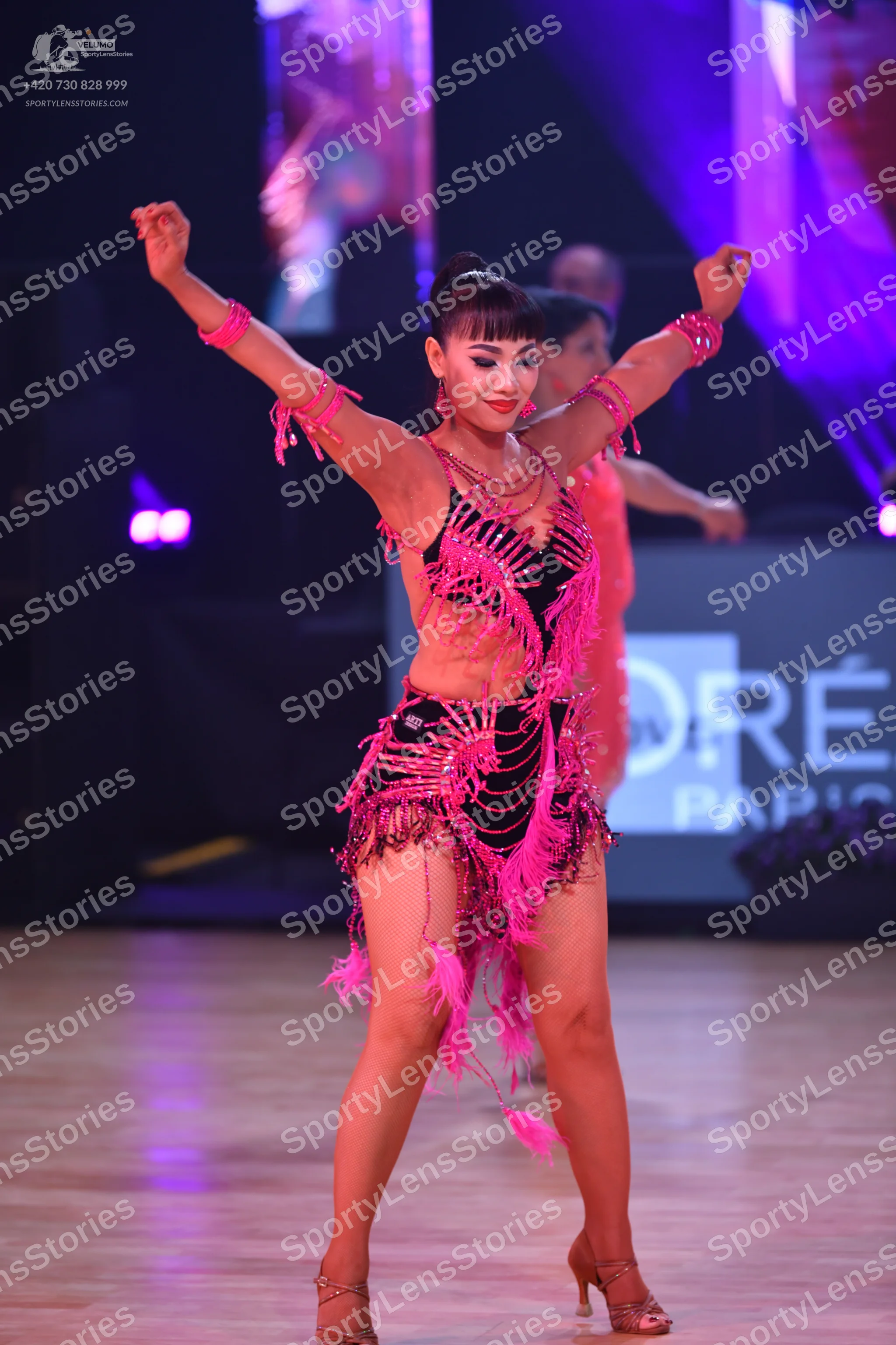 Dancesport competitor: Female dancer: black Latin dance costume with vibrant pink fringe, sequins, and