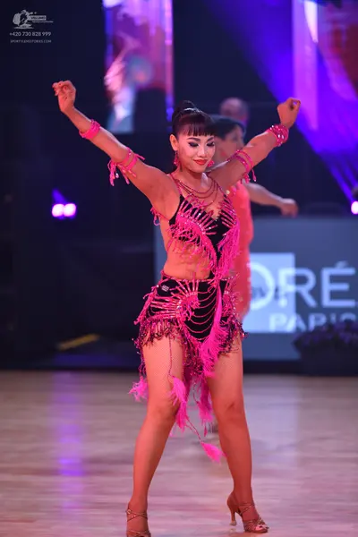 Dancesport competitor: Female dancer: black Latin dance costume with vibrant pink fringe, sequins, and 