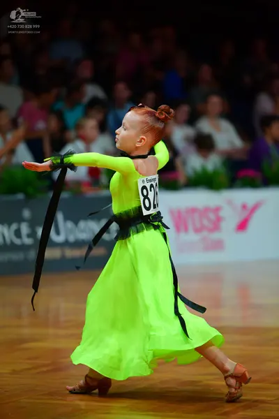 Dancesport competitor: Female dancer: bright lime green ballgown with a black waistband and long, flowi