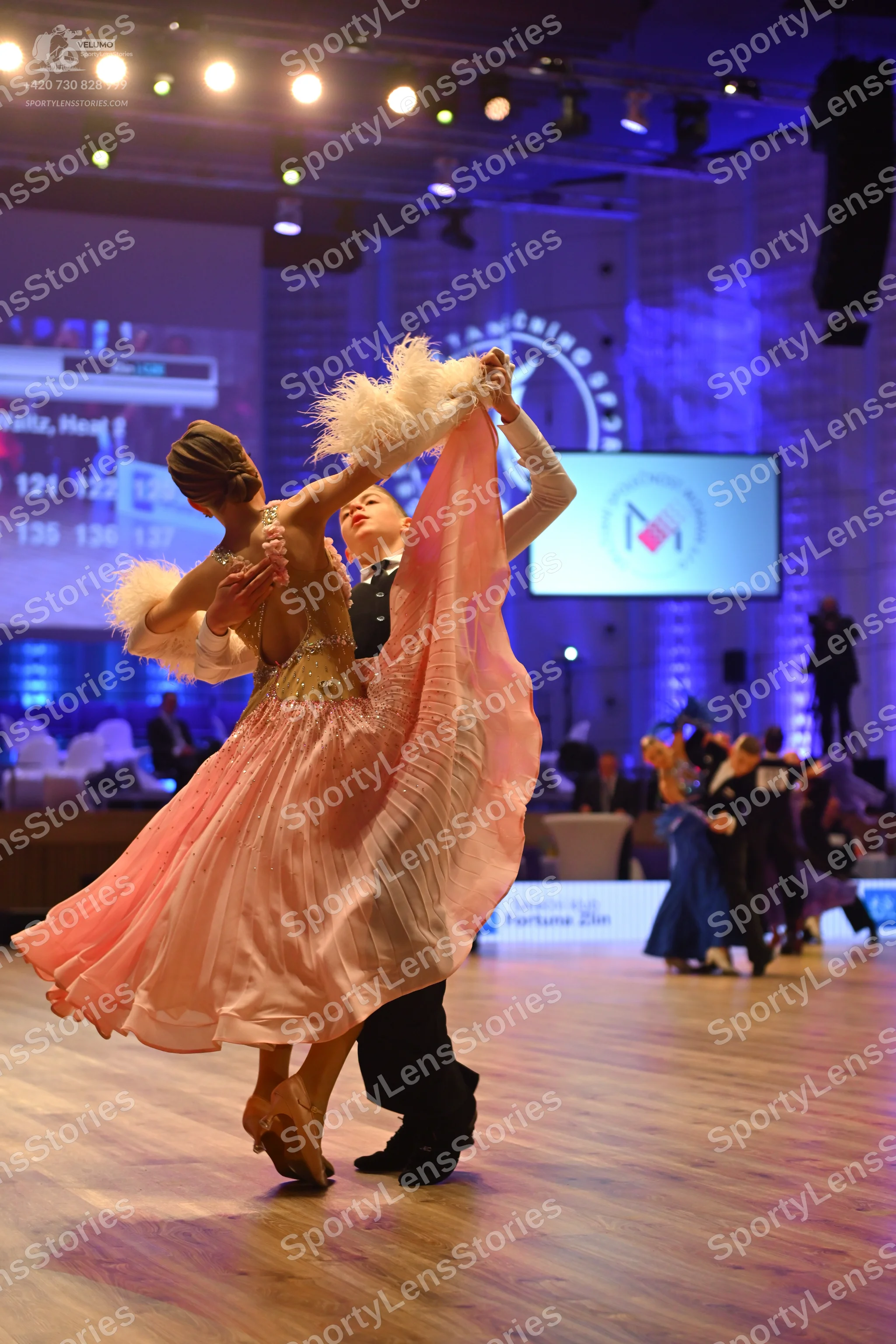 Dancesport competitor: Female dancer: light pink ballgown with a sequined bodice and large white feathe