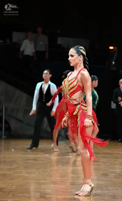Dancesport competitor: Main female dancer: red Latin dress with gold sequin embellishments and long red
