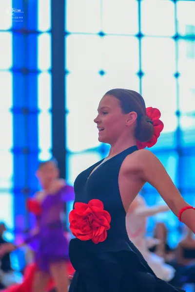 Dancesport competitor: Female dancer in foreground: black Latin dress with a large red fabric rose on t