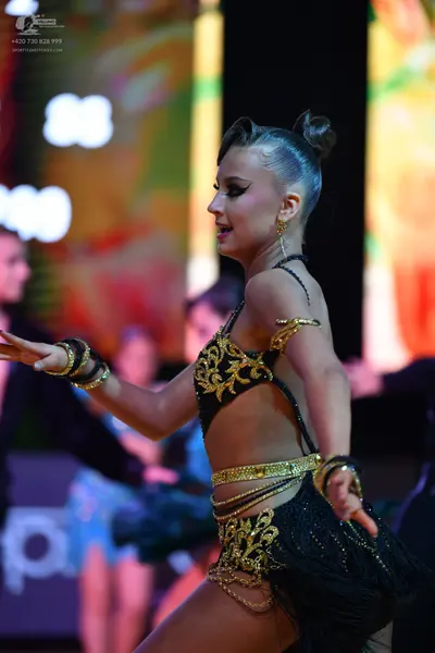 Dancesport competitor: Female dancer in foreground: black Latin dance costume with gold sequin and embr