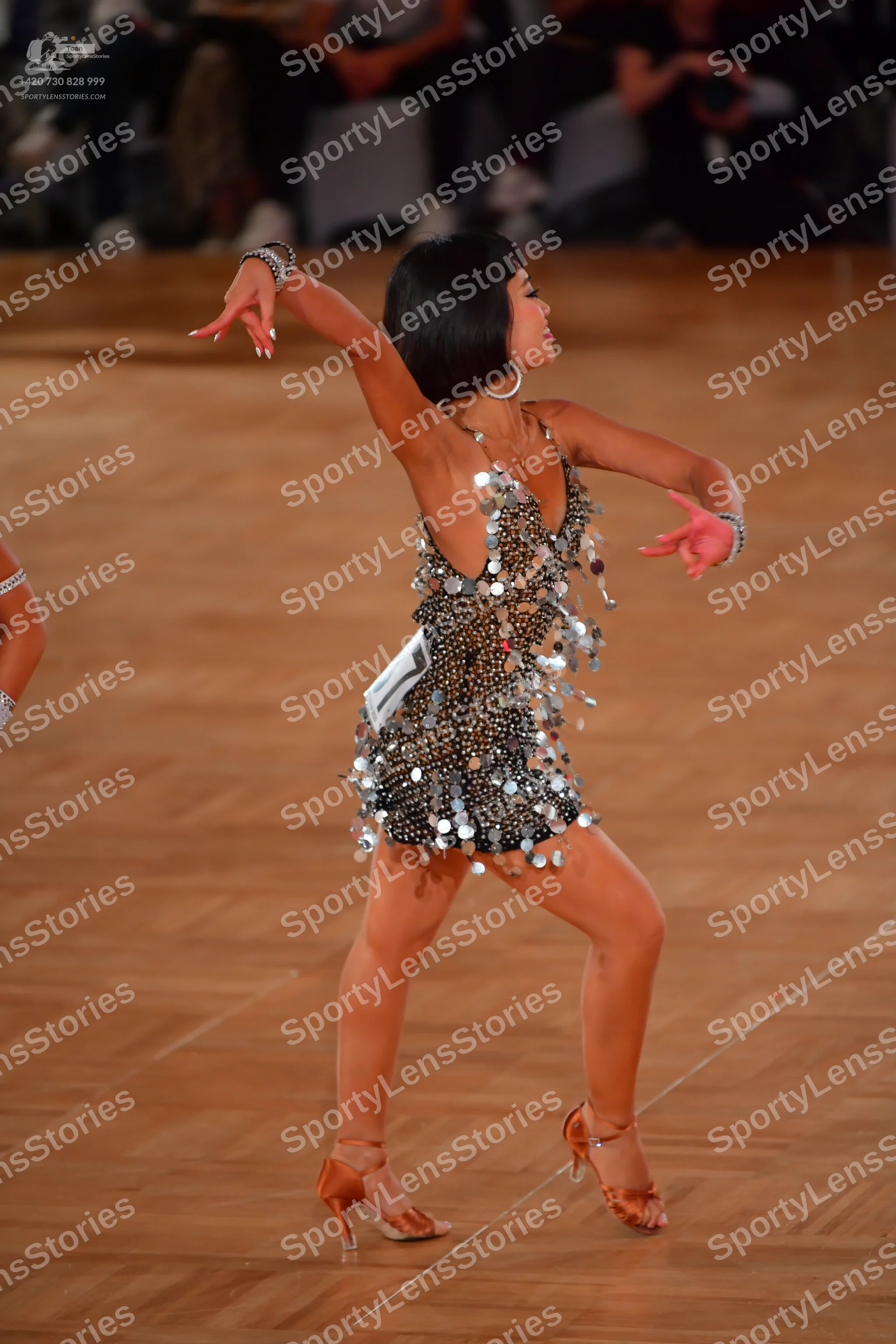 Dancesport competitor: Female dancer: dark Latin dress covered in large silver sequins, with thin strap