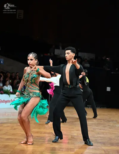 Dancesport competitor: Female dancer: teal Latin dance dress with intricate patterns, cutouts, and long