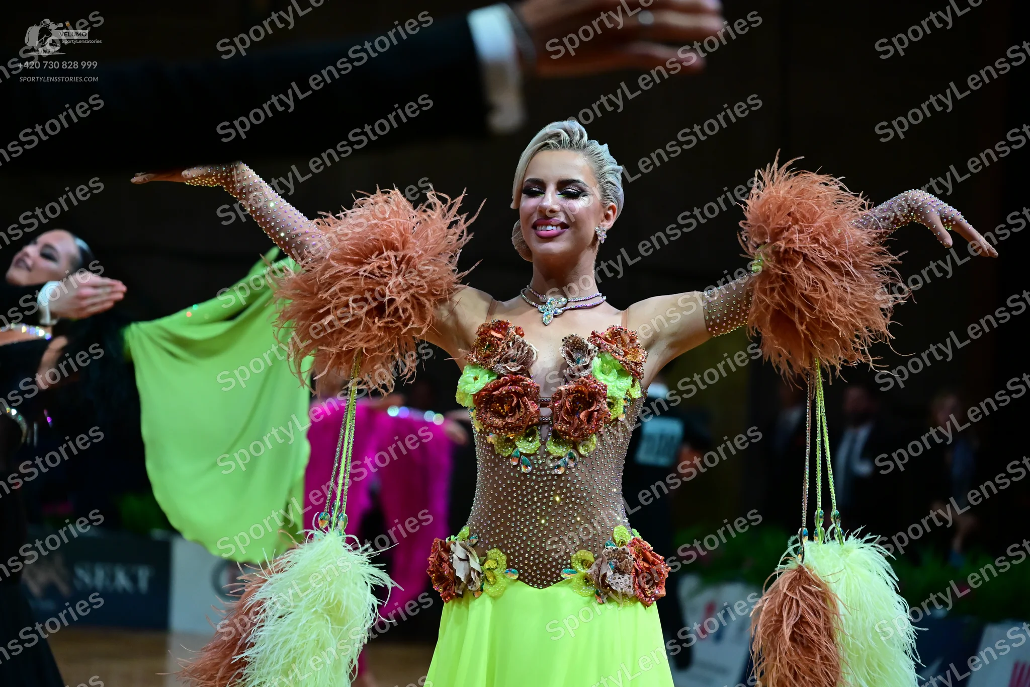 Dancesport competitor: Female dancer in foreground: lime green and tan Latin dance dress with a sequine