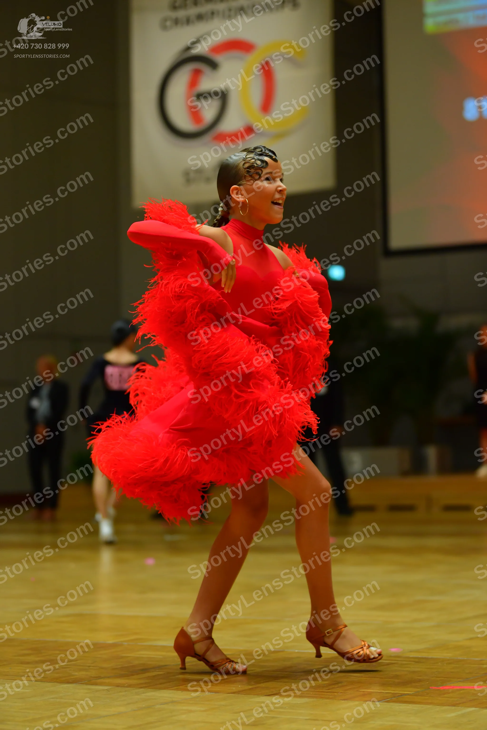 Dancesport competitor: Female dancer: bright red Latin dress with voluminous feather or fringe texture