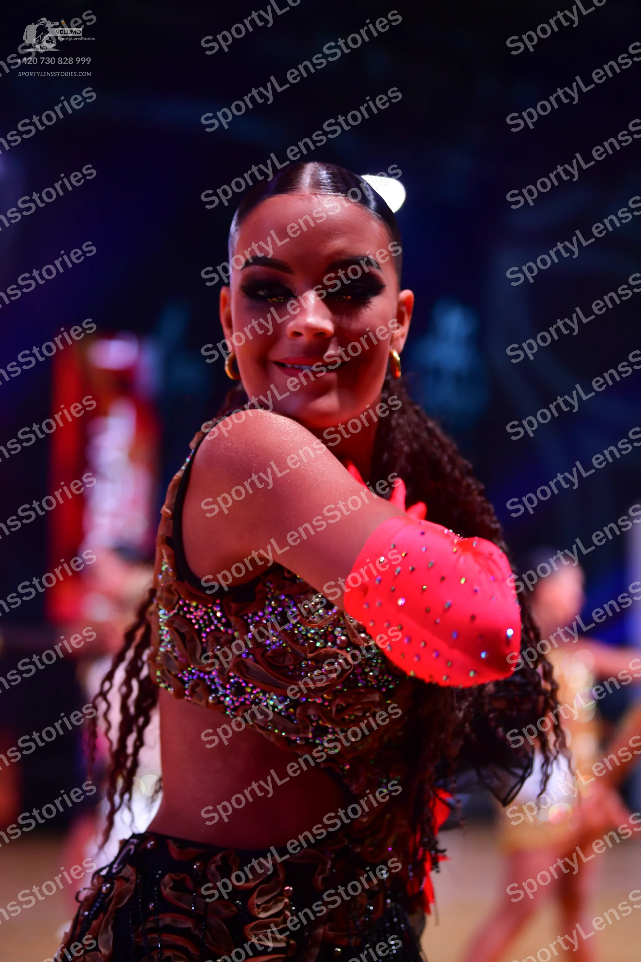 Dancesport competitor: Female dancer in foreground: dark brown or black Latin dance costume with intric