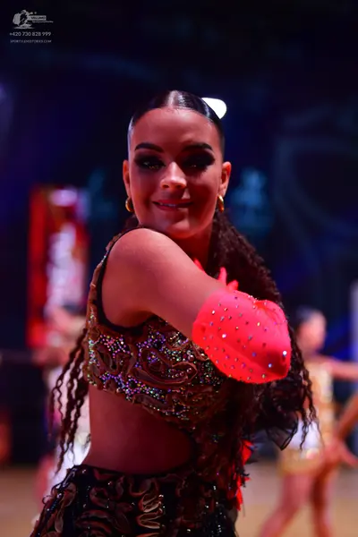 Dancesport competitor: Female dancer in foreground: dark brown or black Latin dance costume with intric