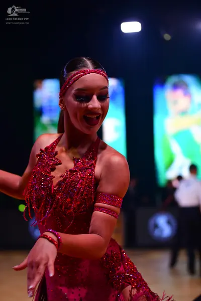 Dancesport competitor: Female dancer: dark red/maroon Latin dress with sequins, fringe, and matching ar