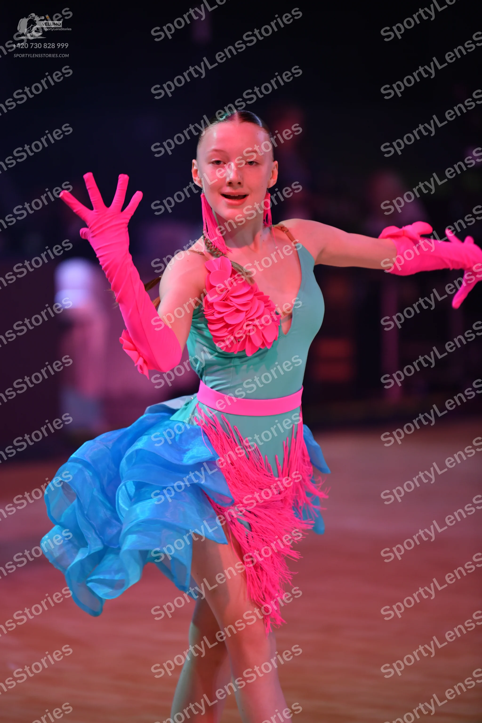 Dancesport competitor: Female dancer: teal Latin dance dress with pink waistband, large pink ruffled fl