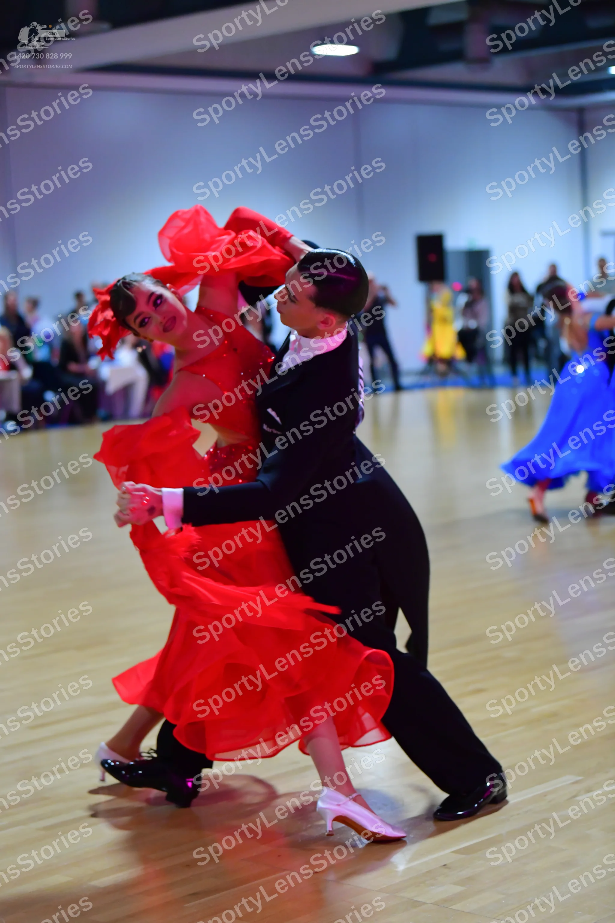 Dancesport competitor: Female dancer in foreground: red latin dress with layered, ruffled skirt and whi