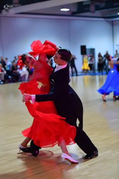 Dancesport competitor: Female dancer in foreground: red latin dress with layered, ruffled skirt and whi