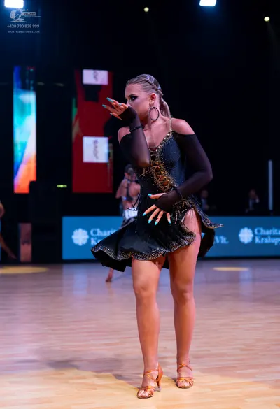 Dancesport competitor: Female dancer: black latin dress with gold embellishments and long mesh sleeves