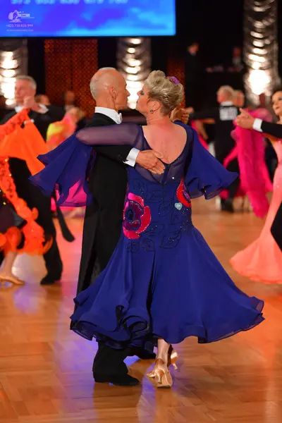 Dancesport competitor: Foreground female dancer: deep purple/blue flowing dress with a large red floral