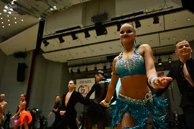 Dancesport competitor: Foreground female dancer: teal/turquoise two-piece Latin costume with a sequined
