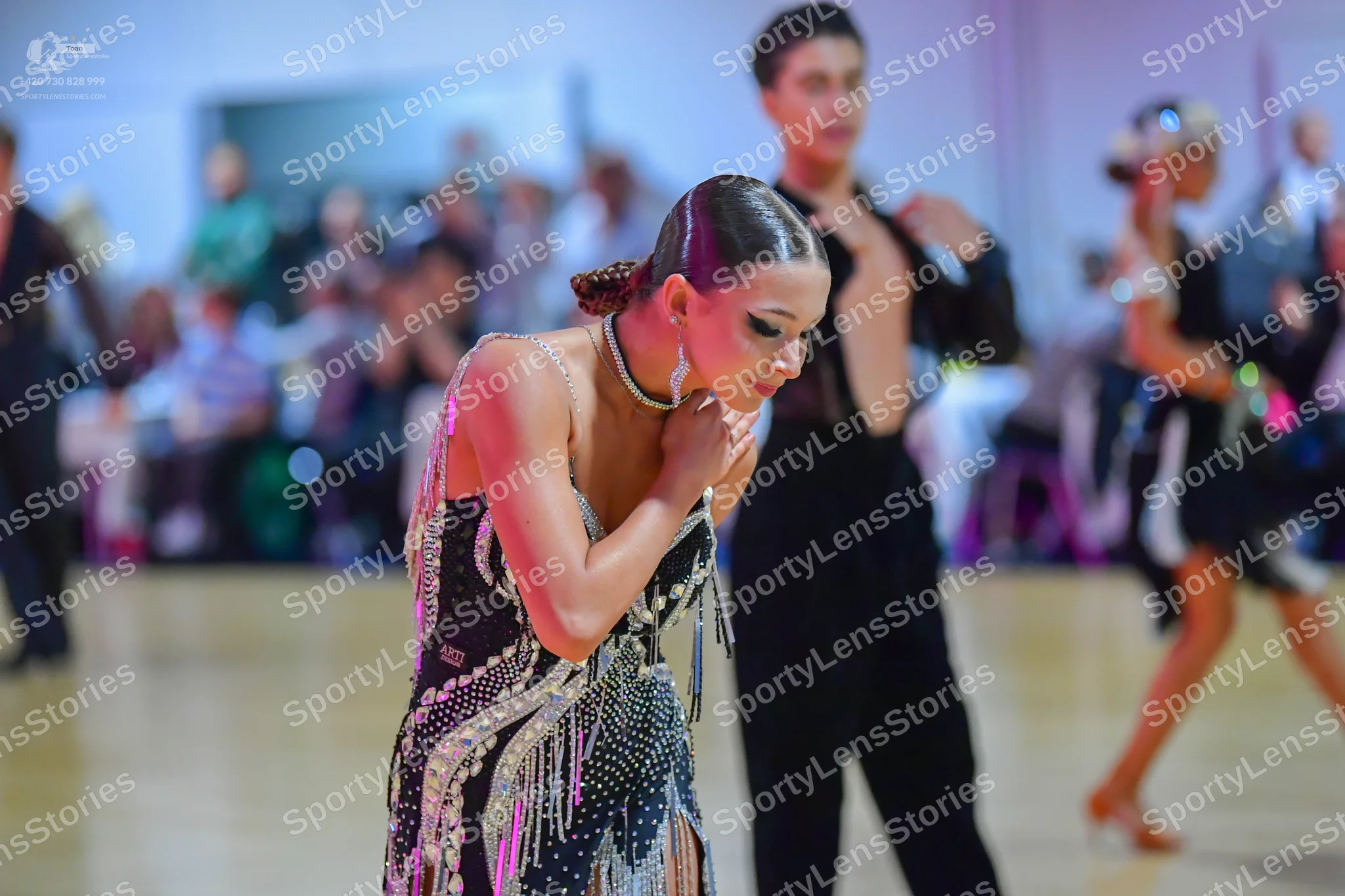 Dancesport competitor: Foreground female dancer: black latin dress heavily embellished with silver sequ