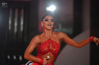 Dancesport competitor #16: Female dancer: red latin dress with lace and cutouts, accessorized with large re