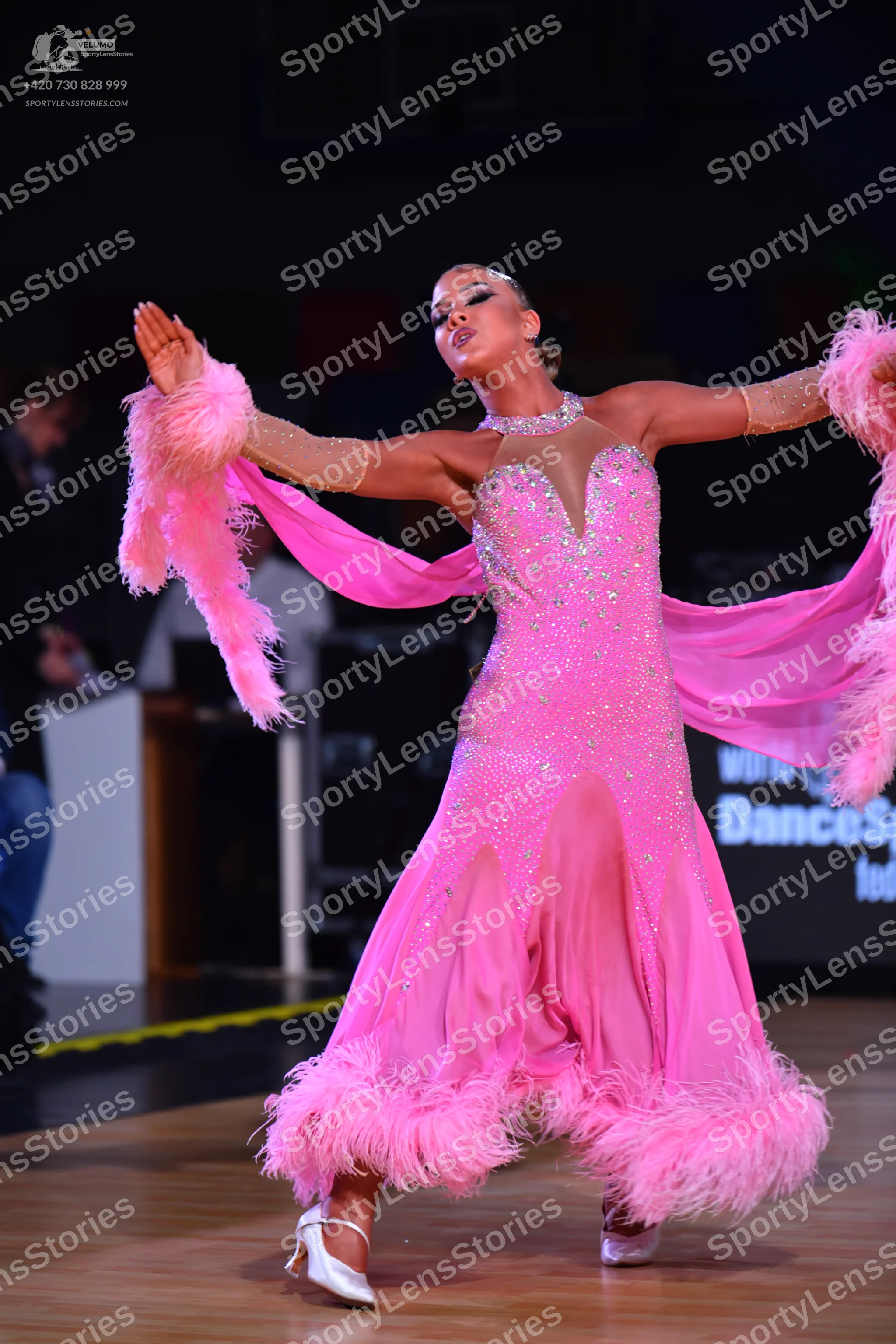 Dancesport competitor: Female dancer: bright pink long flowing dress with a sequined bodice, pink feath