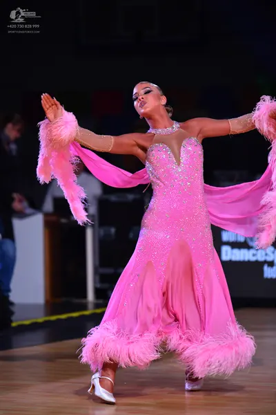 Dancesport competitor: Female dancer: bright pink long flowing dress with a sequined bodice, pink feath