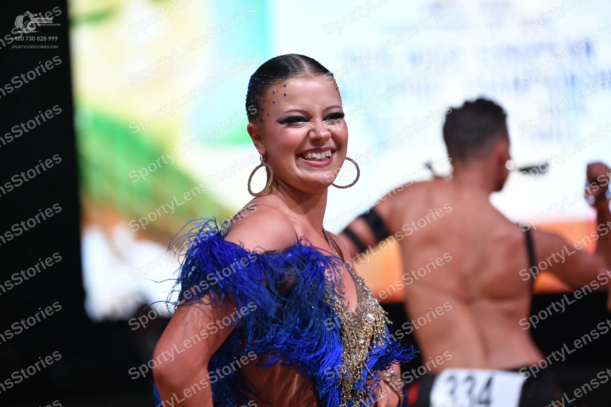 Dancesport competitor: Female dancer: blue and gold Latin dance dress featuring blue feather trim and g