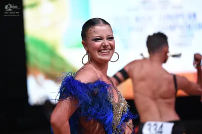 Dancesport competitor: Female dancer: blue and gold Latin dance dress featuring blue feather trim and g