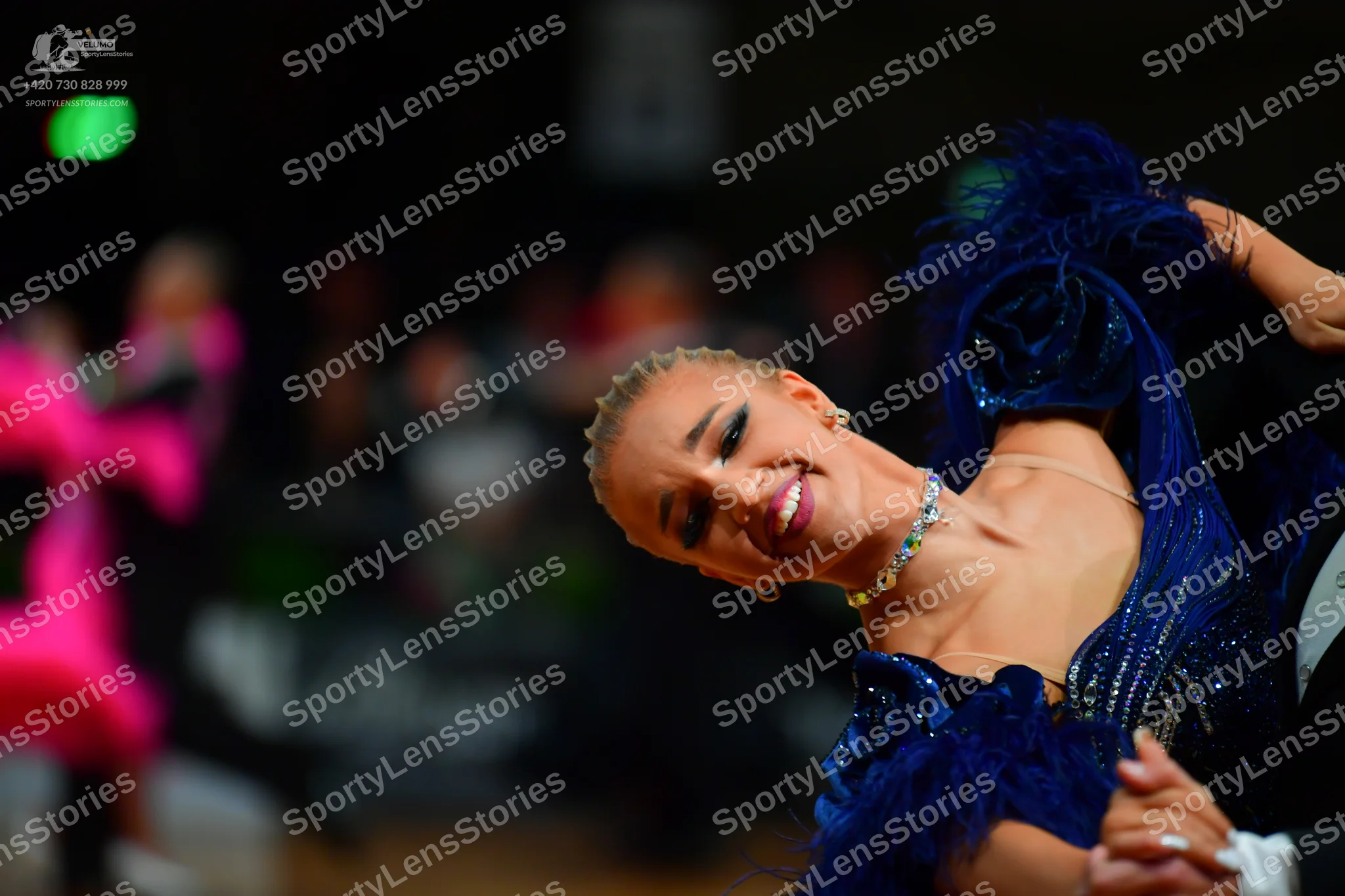 Dancesport competitor: Female dancer in foreground: deep blue Latin dance dress with sequins and feathe