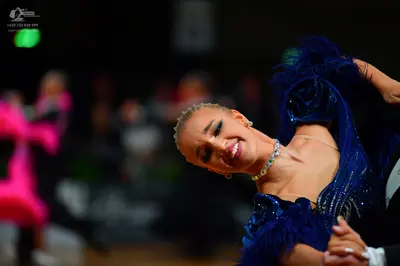 Dancesport competitor: Female dancer in foreground: deep blue Latin dance dress with sequins and feathe