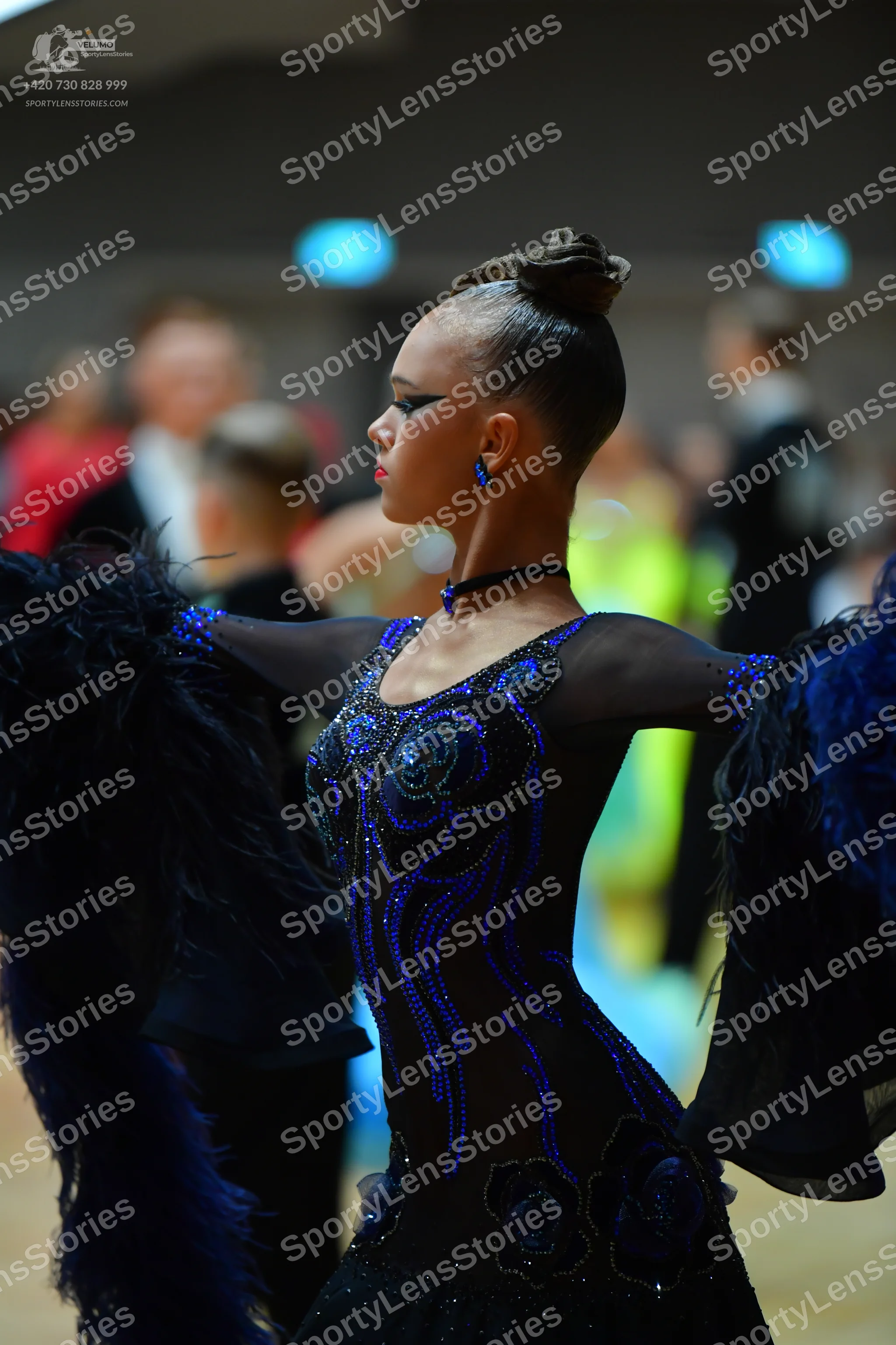 Dancesport competitor: Female dancer: black latin dress with blue sequin patterns, sheer sleeves with l