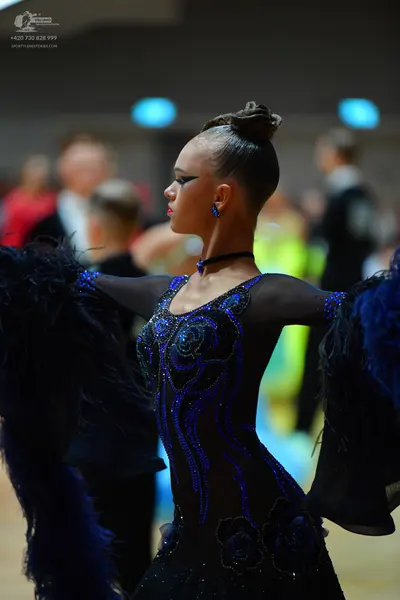 Dancesport competitor: Female dancer: black latin dress with blue sequin patterns, sheer sleeves with l