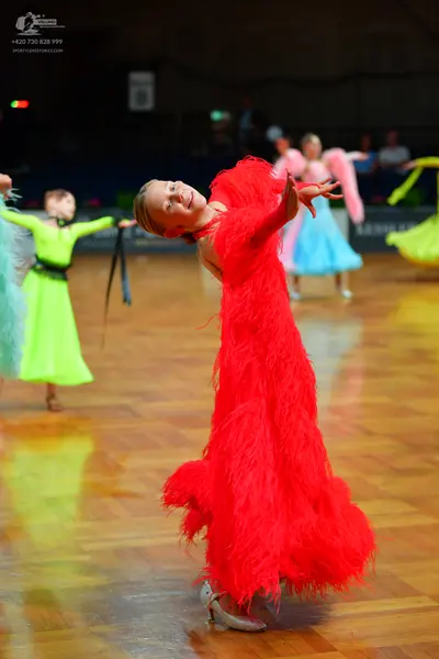 Dancesport competitor: Female dancer in foreground: red latin dress with long fringe