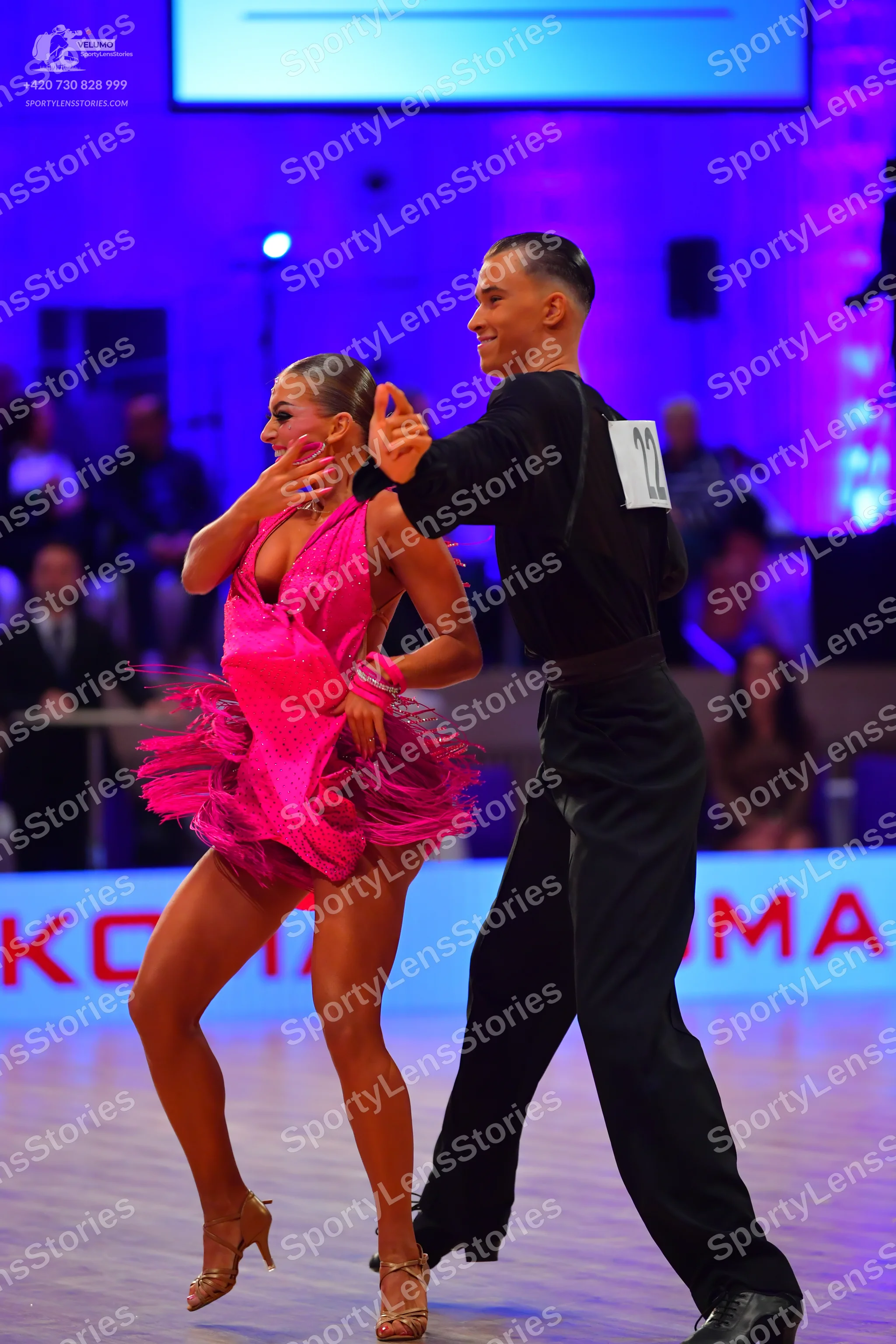 Dancesport competitor: Female dancer: bright pink latin dress with a flared, ruffled skirt and gold str