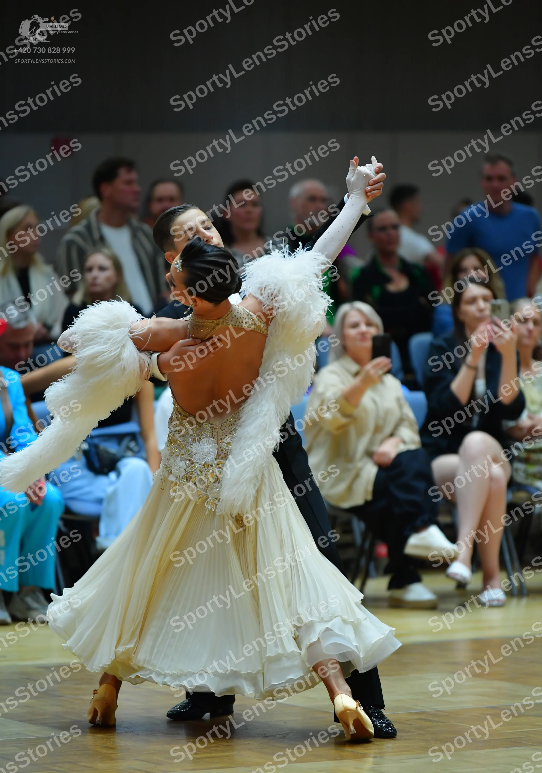 Dancesport competitor: Female dancer: cream-colored ballgown with a sequined bodice, a large white feat