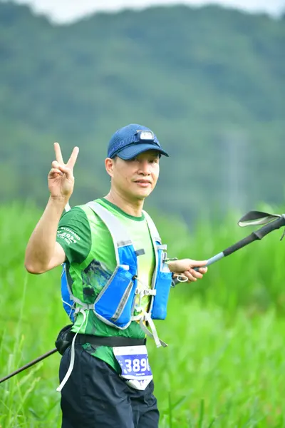 Marathon runner #389: Runner 1: green jersey, blue and white hydration vest, black shorts, blue cap