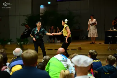 Dancesport competitor: Male dancer: black short-sleeved shirt with a green and teal floral pattern and 