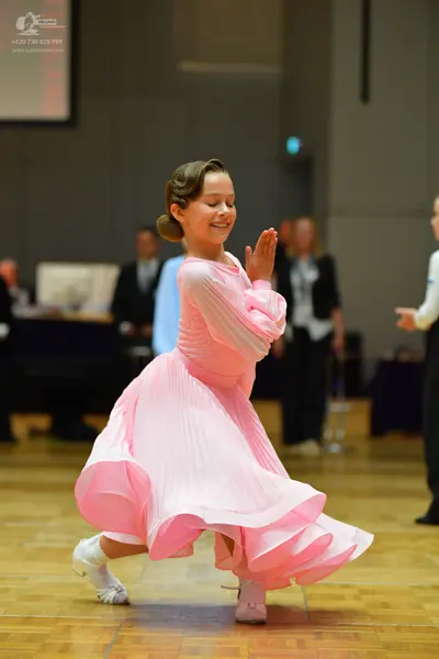 Dancesport competitor: Female dancer: pink ballroom dress with a voluminous ruffled skirt and pleated b