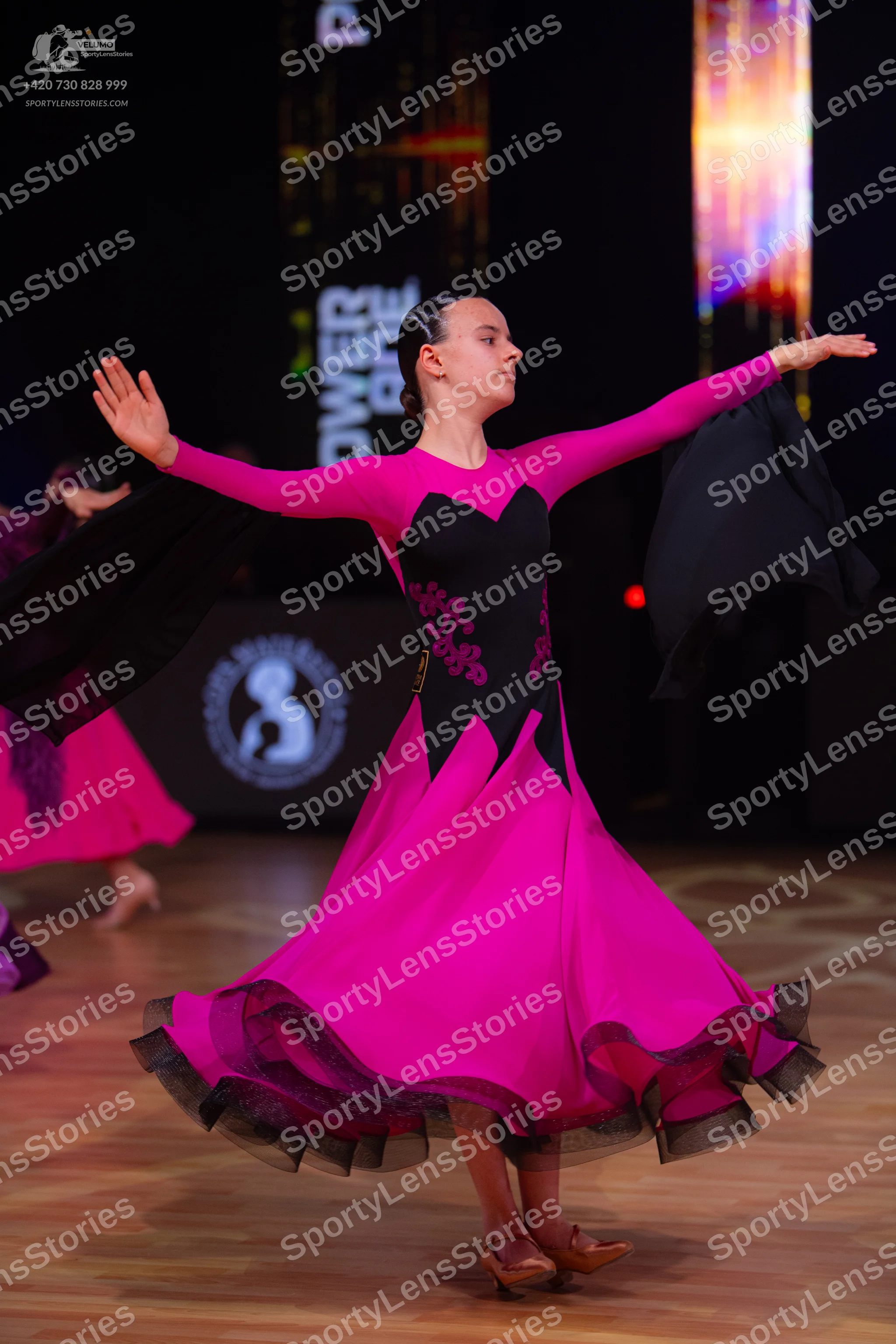 Dancesport competitor: Female dancer: pink and black ballroom dress with long sleeves, a black bodice f