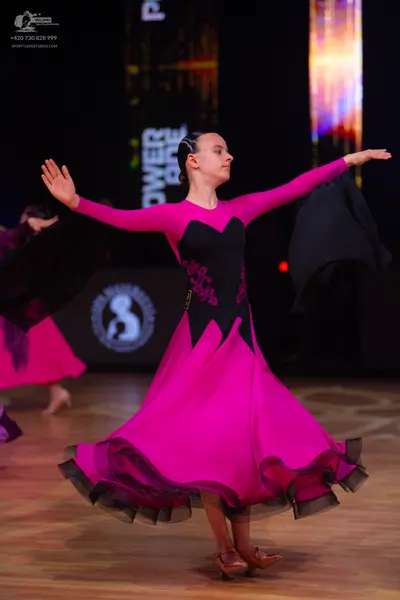 Dancesport competitor: Female dancer: pink and black ballroom dress with long sleeves, a black bodice f