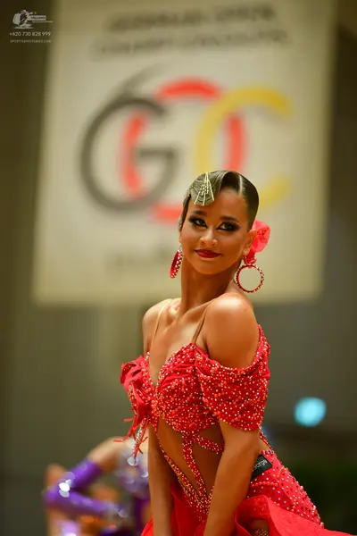 Dancesport competitor: Female dancer in foreground: red Latin dance dress with rhinestones and cutouts,