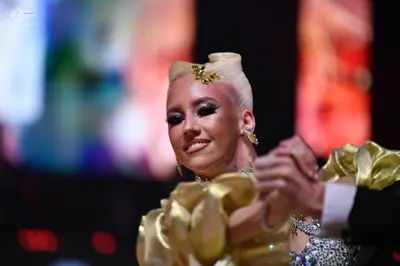 Dancesport competitor: Female dancer: gold-colored costume with voluminous, ruffled satin-like sleeves 