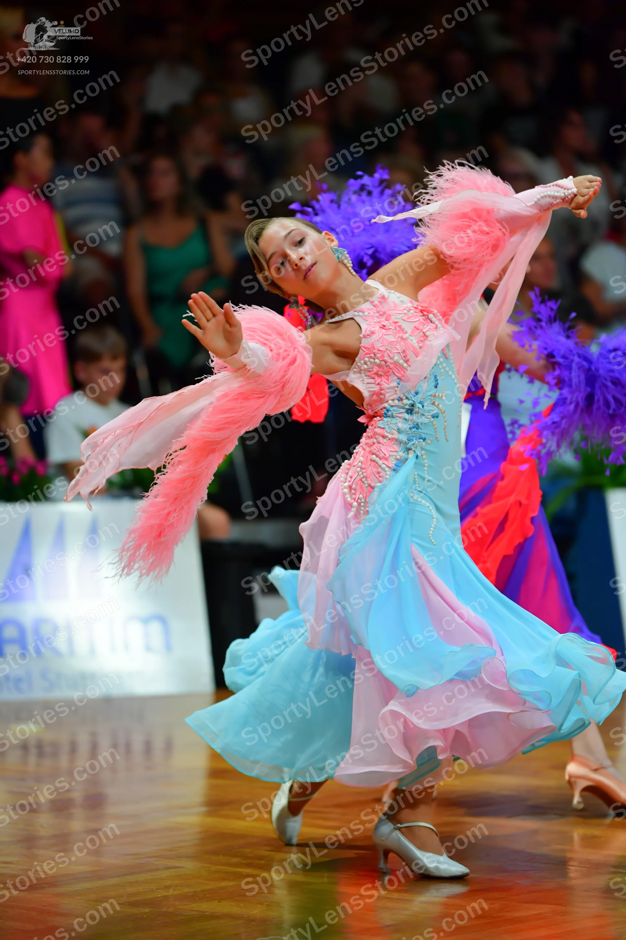 Dancesport competitor: Main female dancer: light blue and pink ballgown with a voluminous, multi-layere