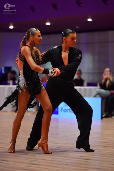 Dancesport competitor: Female dancer: black Latin dress with sequins and fringe, large hoop earrings, a